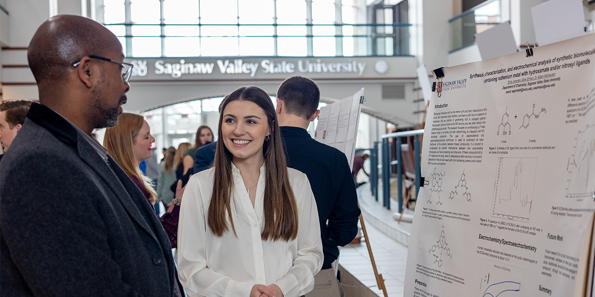 A student being mentored by a professor while giving a presentation